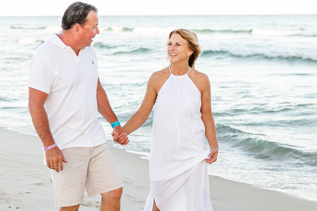 Couple holding hands walking down the beach by the water